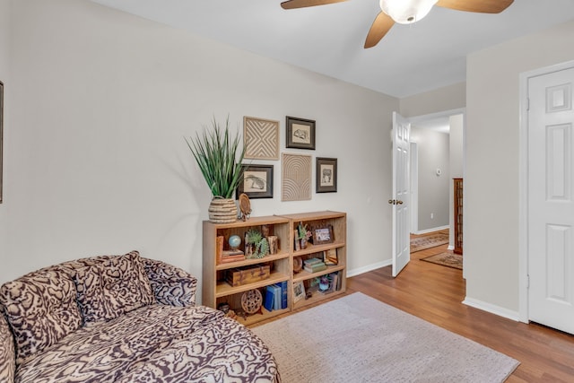 living area with baseboards, a ceiling fan, and wood finished floors
