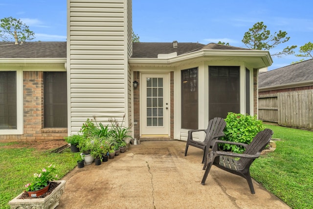 view of exterior entry with a chimney, roof with shingles, fence, a yard, and a patio