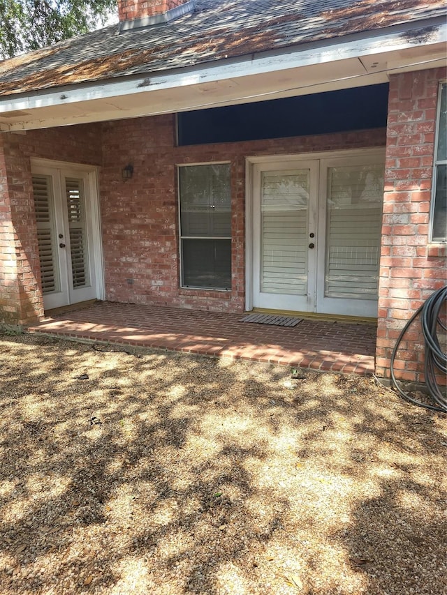 view of exterior entry featuring brick siding, roof with shingles, and french doors