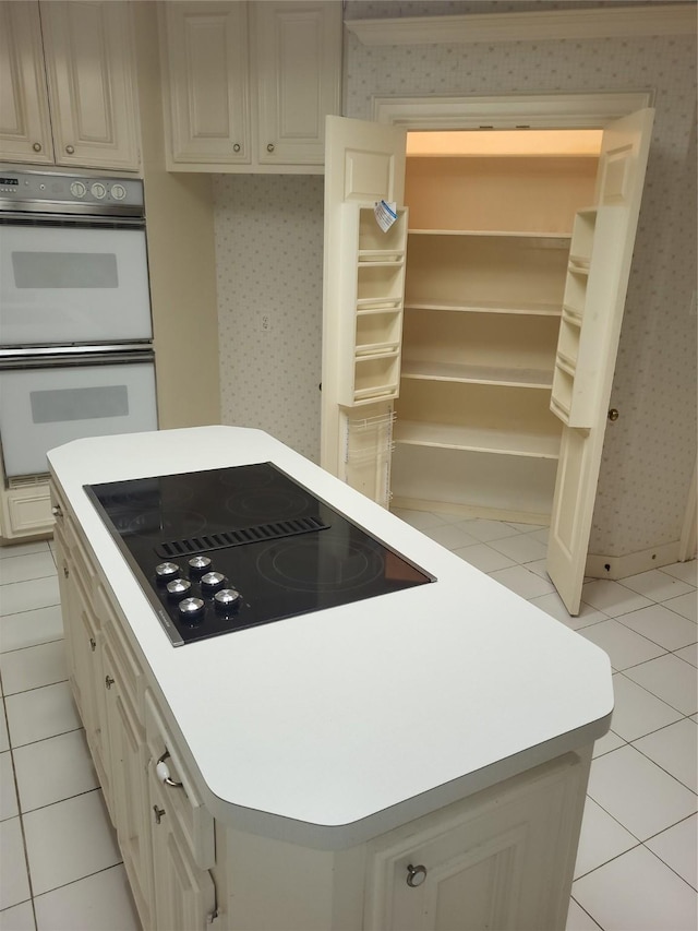 kitchen featuring double oven, black electric stovetop, wallpapered walls, light countertops, and light tile patterned floors