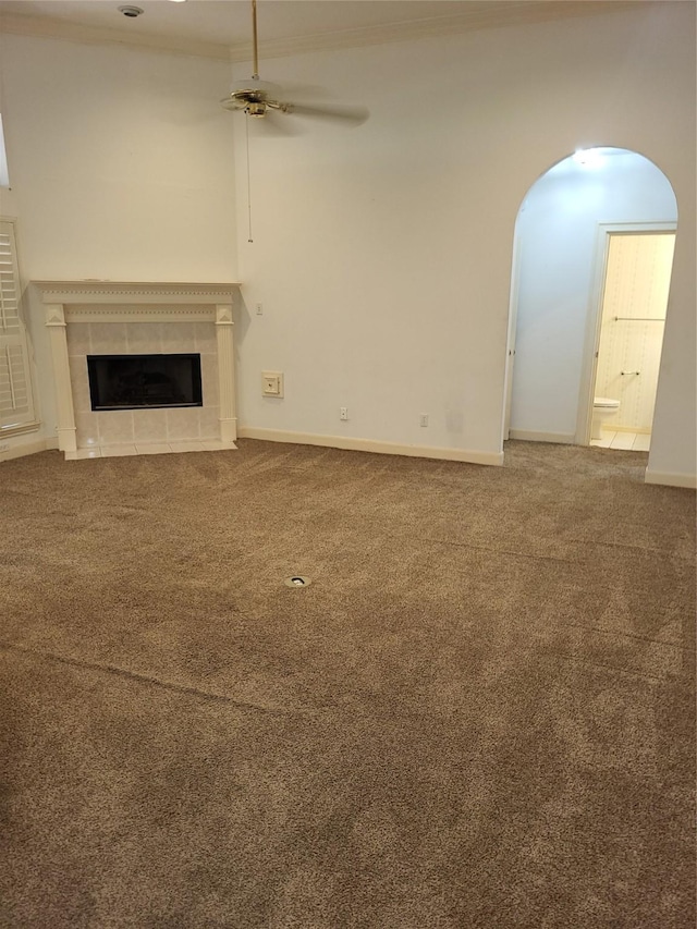 unfurnished living room featuring ceiling fan, crown molding, arched walkways, a tile fireplace, and carpet floors