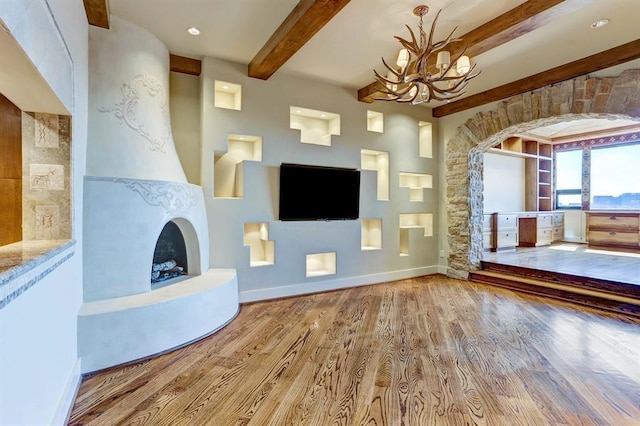 unfurnished living room with wood finished floors, beamed ceiling, baseboards, a large fireplace, and a notable chandelier