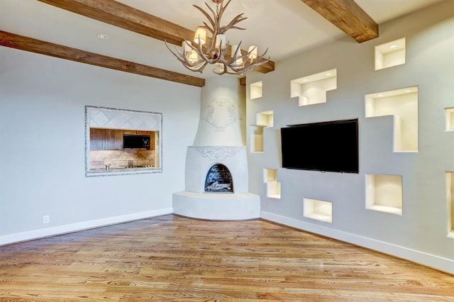 unfurnished living room with an inviting chandelier, beam ceiling, baseboards, wood finished floors, and a high end fireplace