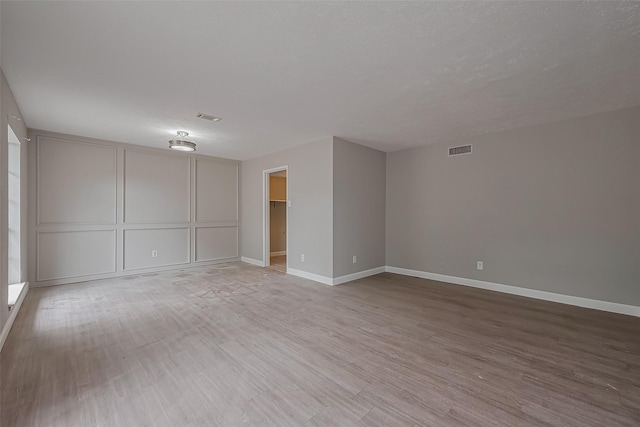 spare room with baseboards, a decorative wall, light wood-type flooring, and visible vents
