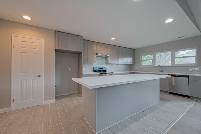 kitchen featuring decorative backsplash, light countertops, gray cabinets, under cabinet range hood, and appliances with stainless steel finishes