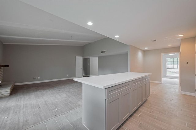 kitchen with gray cabinets, a kitchen island, light countertops, baseboards, and light wood-style flooring