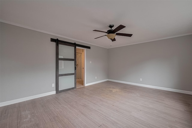 empty room featuring baseboards, a barn door, a ceiling fan, and wood finished floors