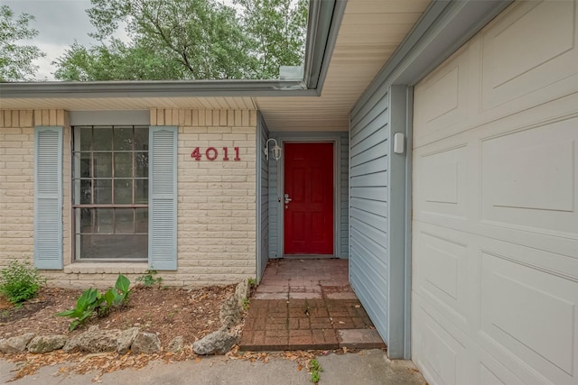 view of exterior entry featuring an attached garage and brick siding