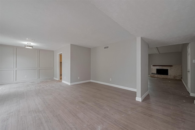 unfurnished living room with baseboards, visible vents, wood finished floors, and a fireplace