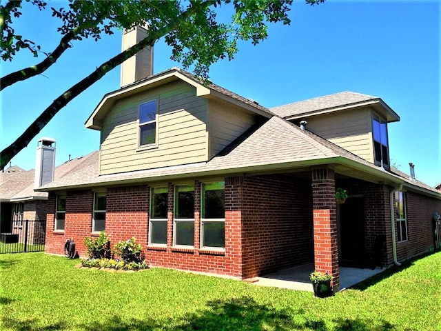 back of house with brick siding, a patio, a yard, and a chimney