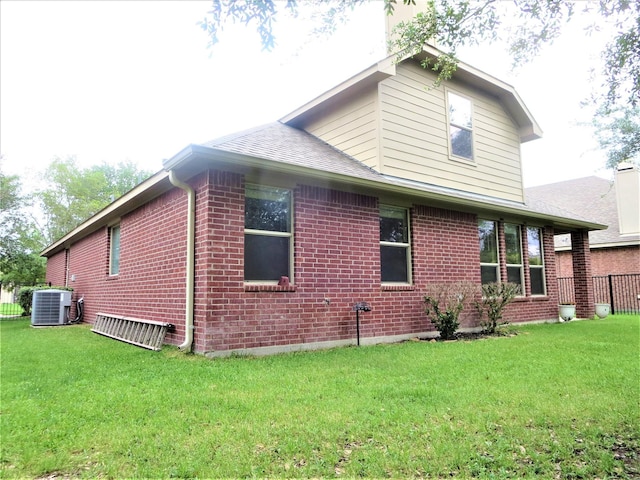 view of side of home featuring fence, a shingled roof, central AC, brick siding, and a yard
