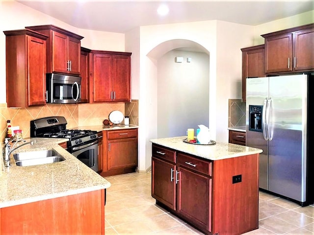 kitchen featuring light stone counters, a sink, arched walkways, stainless steel appliances, and reddish brown cabinets