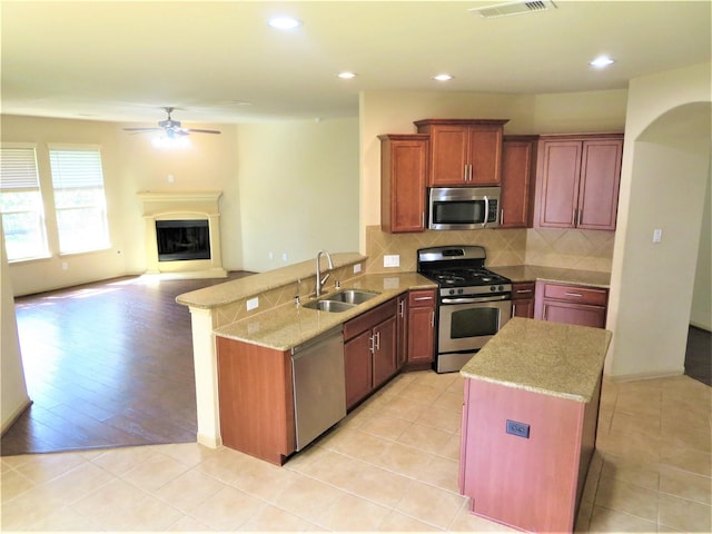 kitchen featuring a sink, a peninsula, tasteful backsplash, a ceiling fan, and appliances with stainless steel finishes
