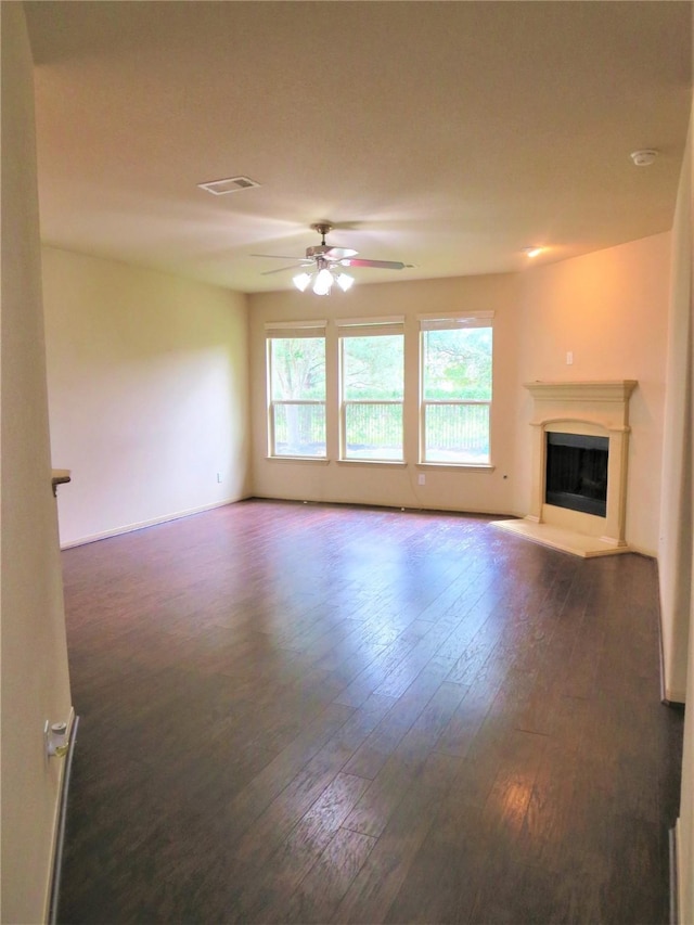 unfurnished living room with a ceiling fan, dark wood-type flooring, a fireplace with raised hearth, and visible vents