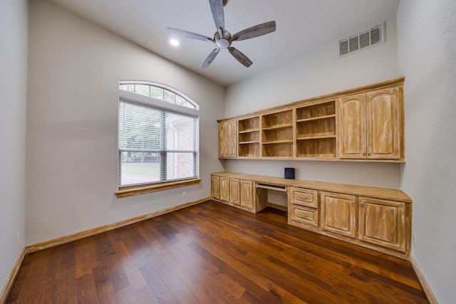 unfurnished office with a ceiling fan, visible vents, built in desk, baseboards, and dark wood-style floors