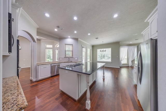 kitchen with white cabinets, dark wood finished floors, stainless steel appliances, a kitchen island, and visible vents