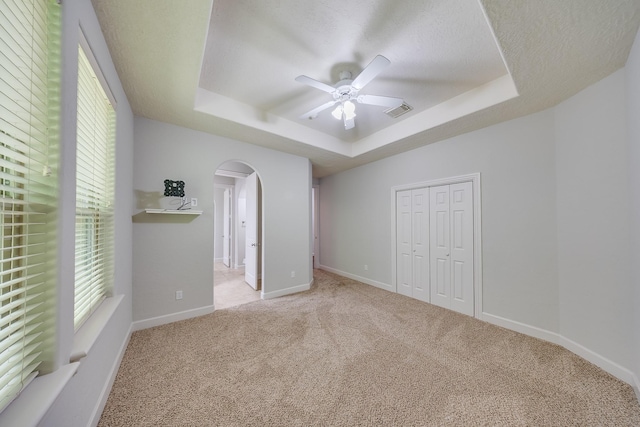 unfurnished bedroom with visible vents, arched walkways, a raised ceiling, carpet floors, and a closet
