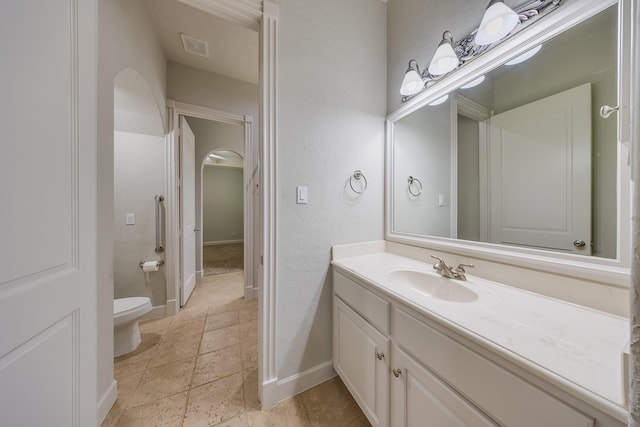 bathroom featuring vanity, toilet, stone tile floors, baseboards, and visible vents