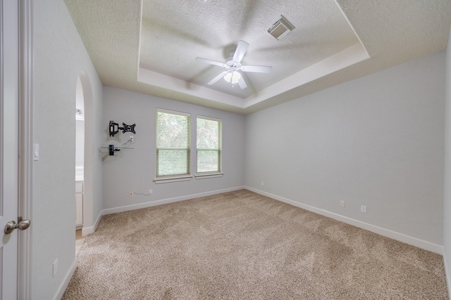 unfurnished room with ceiling fan, a textured ceiling, visible vents, a raised ceiling, and light carpet