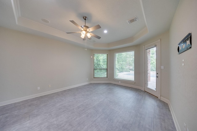 spare room featuring visible vents, plenty of natural light, a tray ceiling, and ceiling fan