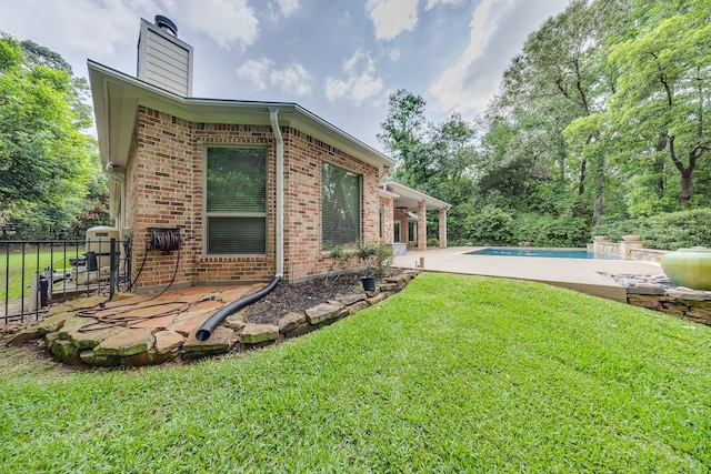 rear view of house with a chimney, an outdoor pool, brick siding, a yard, and a patio