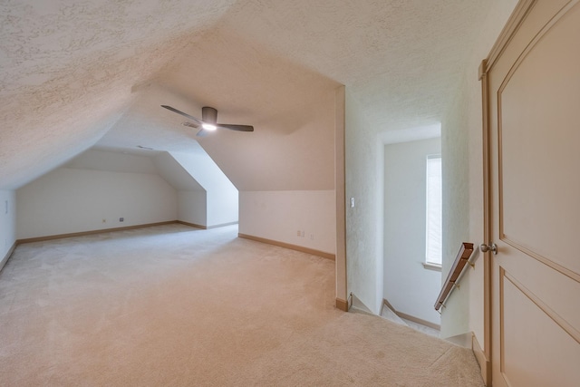 additional living space featuring baseboards, ceiling fan, light colored carpet, a textured ceiling, and vaulted ceiling