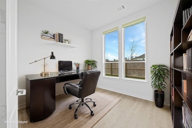 office space featuring light wood-style floors, baseboards, lofted ceiling, and visible vents