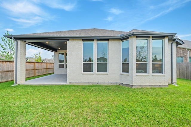 back of property featuring a patio area, brick siding, fence, a yard, and a shingled roof