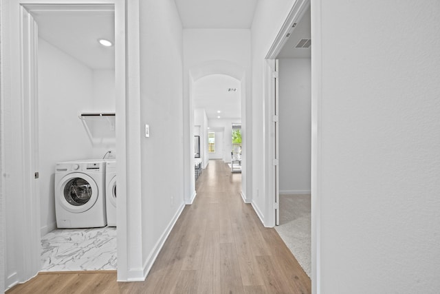 corridor with visible vents, arched walkways, washing machine and dryer, light wood-type flooring, and baseboards
