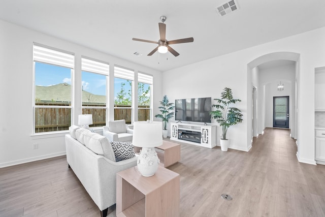 living area with ceiling fan, arched walkways, light wood-style flooring, baseboards, and visible vents