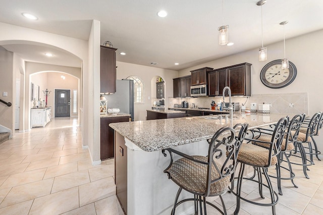 23414 Bracino Lake Dr, Katy, TX 77493 - kitchen featuring appliances with stainless steel finishes, arched walkways, dark brown cabinets, a peninsula, and a breakfast bar