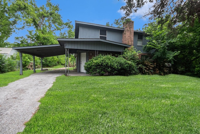 view of front of home with an attached carport, driveway, a front yard, and a chimney