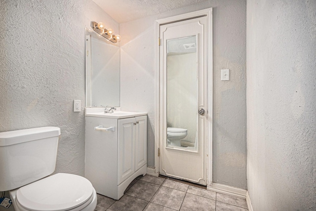 bathroom featuring toilet, a textured wall, tile patterned flooring, and vanity