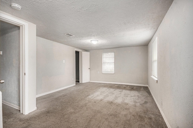 spare room with carpet flooring, a textured ceiling, visible vents, and plenty of natural light
