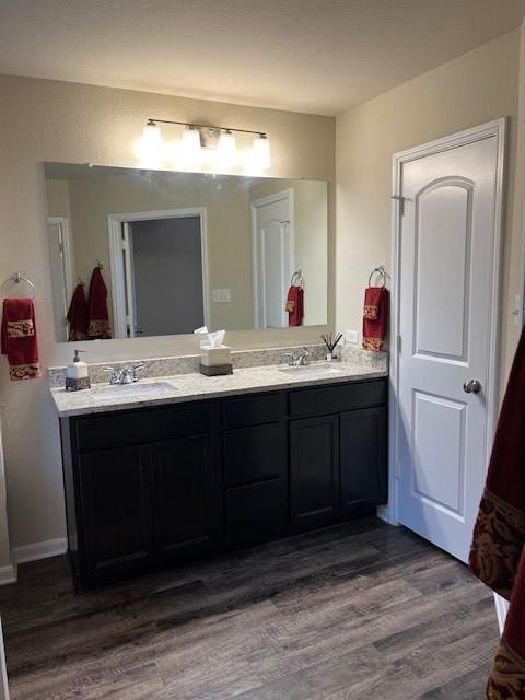 full bath with a sink, double vanity, and wood finished floors