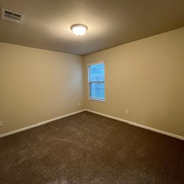 unfurnished room featuring visible vents, a textured ceiling, baseboards, and dark carpet