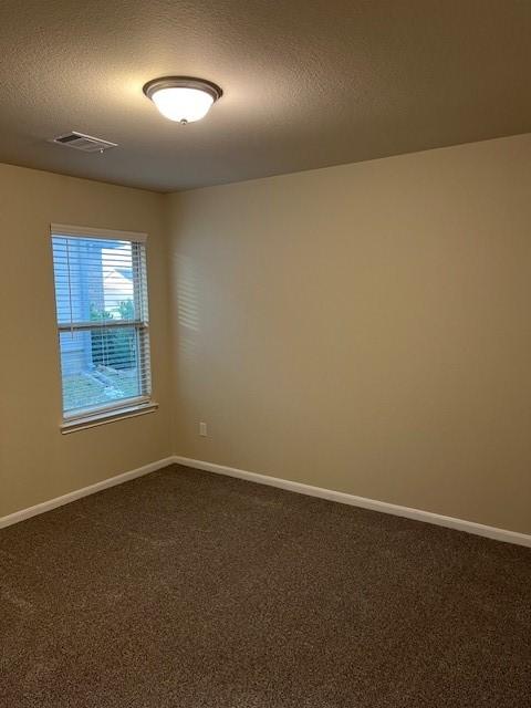empty room with dark carpet, a textured ceiling, baseboards, and visible vents