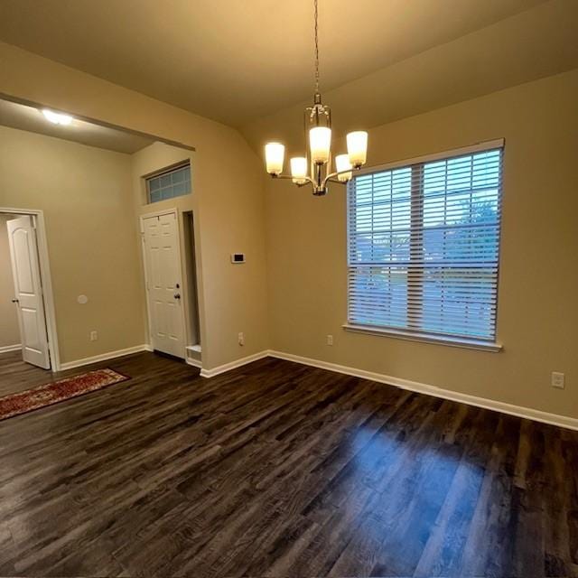 empty room featuring baseboards, an inviting chandelier, dark wood finished floors, and lofted ceiling