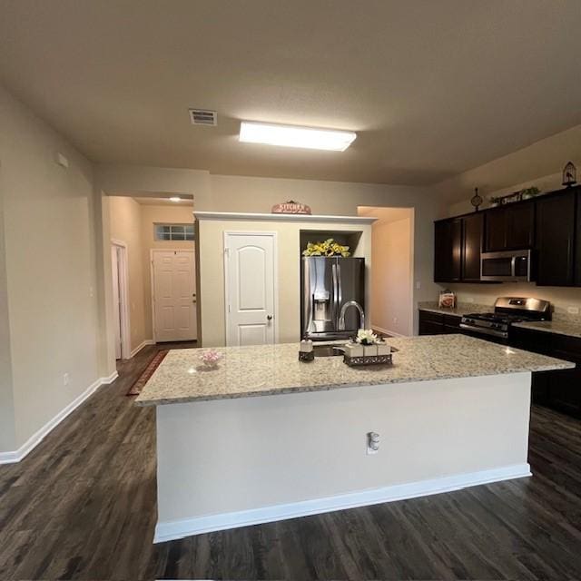 kitchen featuring light stone countertops, appliances with stainless steel finishes, a kitchen island with sink, visible vents, and dark wood-style floors