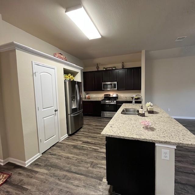 kitchen with dark wood-style flooring, visible vents, a sink, baseboards, and stainless steel appliances