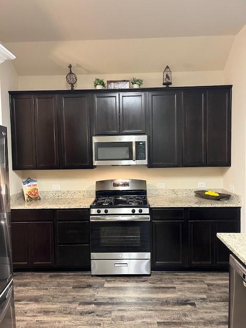 kitchen with light stone counters, dark cabinetry, stainless steel appliances, and wood finished floors
