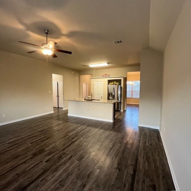 unfurnished living room with dark wood-style flooring, baseboards, visible vents, and a ceiling fan