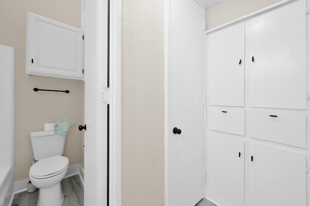 bathroom with toilet, baseboards, and wood finished floors