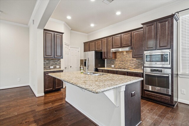 2707 Kings Retreat Cir, Kingwood, TX 77345 - kitchen with dark brown cabinets, a center island with sink, dark wood-type flooring, a sink, and appliances with stainless steel finishes