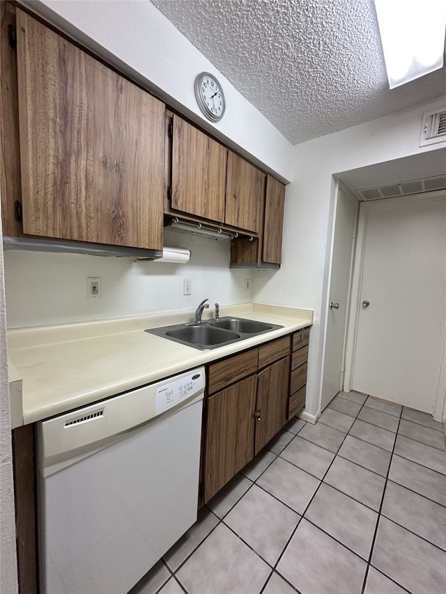 kitchen with white dishwasher, light countertops, light tile patterned floors, and a sink