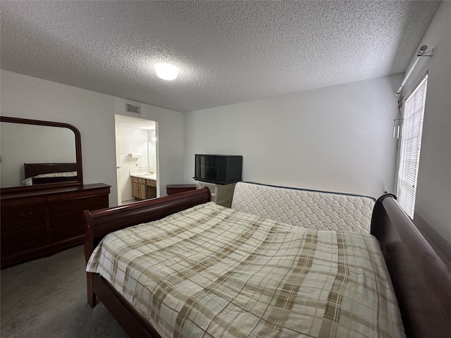 carpeted bedroom with ensuite bathroom, a textured ceiling, and visible vents
