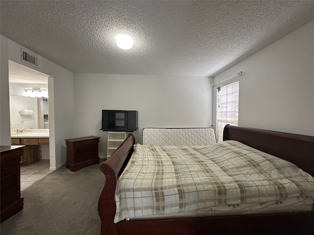 bedroom featuring visible vents, a textured ceiling, ensuite bath, and light carpet