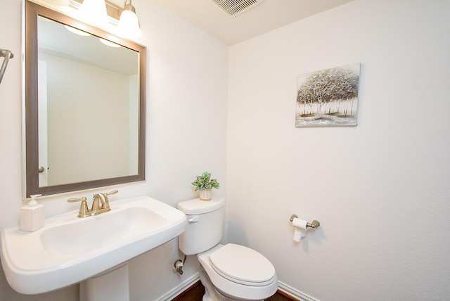 half bath featuring a sink, baseboards, toilet, and visible vents