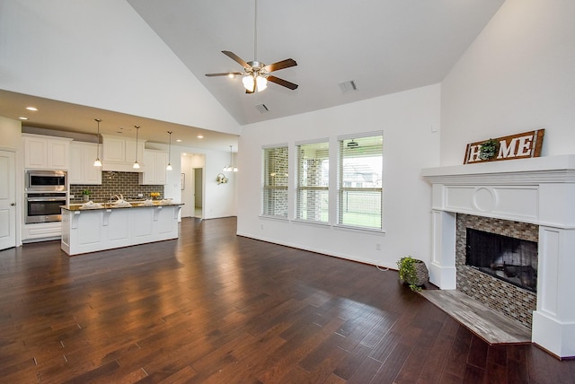 living area with a ceiling fan, visible vents, a fireplace, dark wood finished floors, and high vaulted ceiling