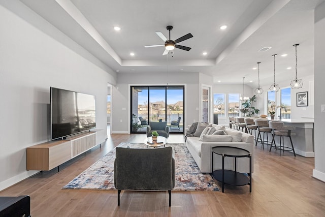 living area with a tray ceiling, baseboards, a ceiling fan, and wood finished floors